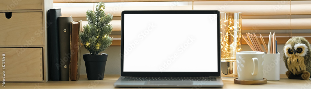 Obraz premium Front view of laptop with white blank display, coffee cup, books and potted plant on wooden counter in cozy home