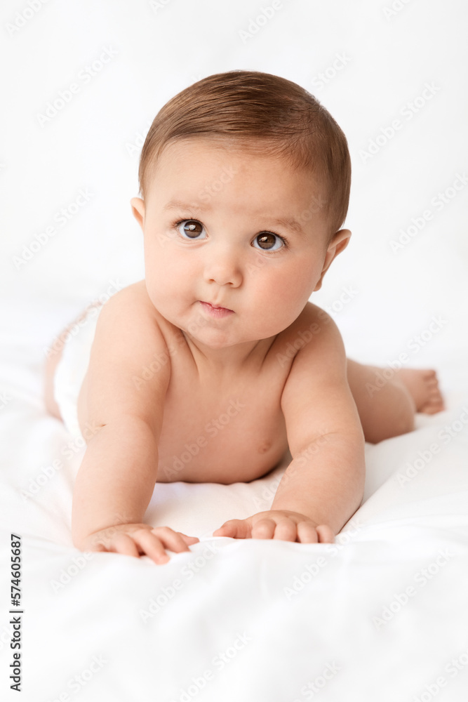 Baby with funny serious expression lying on stomach on white bed Baby with funny serious expression lying on stomach on white bed