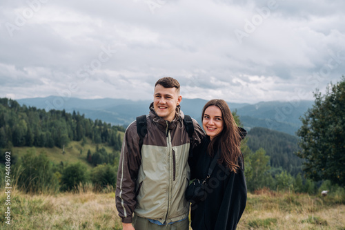 Positive couple of tourists standing in the mountains during a hike and hugging each other with a smile on their face.