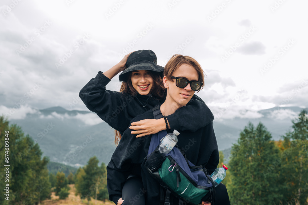 Photo of a beautiful young couple of tourists in the mountains during a hike, hugging and posing for the camera against the background of unreal views.