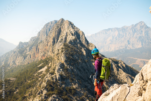girl climber in a helmet and with a backpack stands on a mountain range against the backdrop of mountains and the sky. mountain climbing