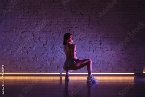 Photo of attractive female dancer in sexy clothes posing for camera against wall background in pink light. © bodnarphoto