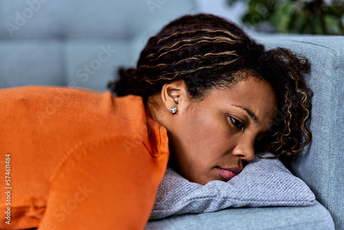 Depressed  African woman tormented by restless sleep, lying on a sofa, looking sad.