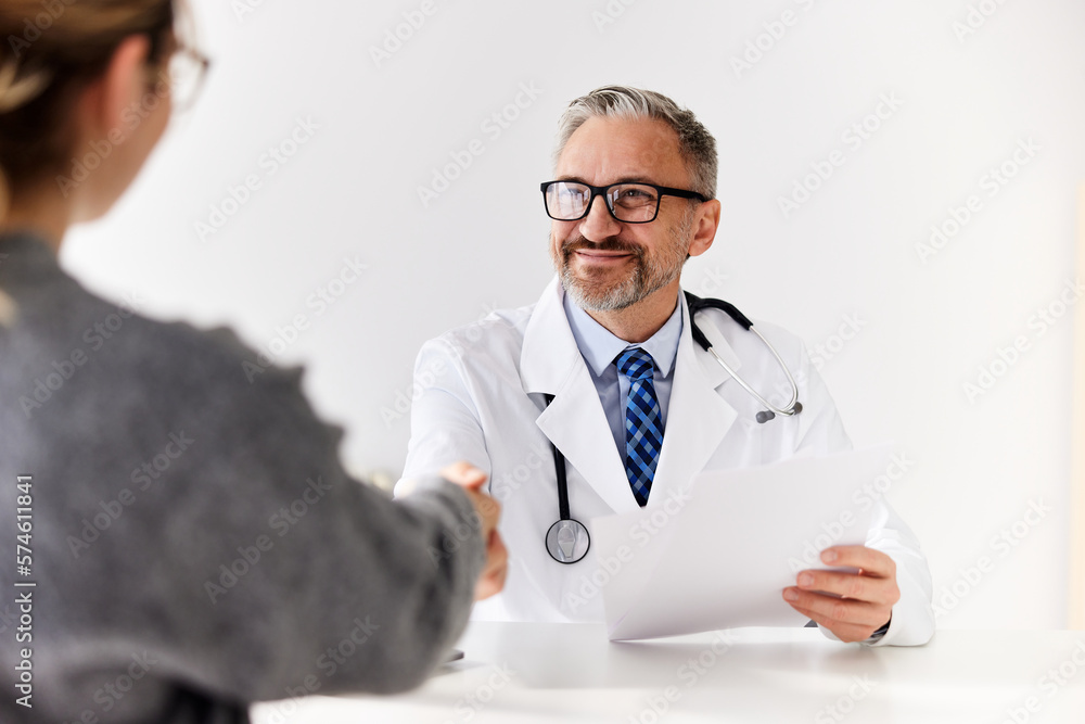 A senior male doctor handshake with a female patient, sitting at the clinic. A senior male doctor handshake with a female patient, sitting at the clinic.