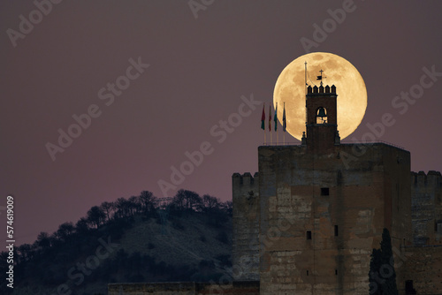 Night photo of Alhambra illuminated by full moon, Torre de la Vela in foreground. Evokes mystery and wonder. Ideal for relevant projects. #574619009