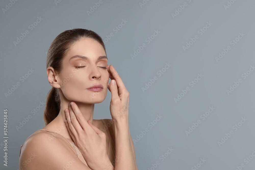 Woman massaging her face on grey background. Space for text Woman massaging her face on grey background. Space for text