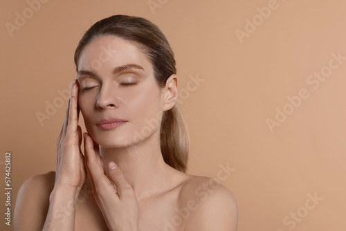 Woman massaging her face on beige background. Space for text