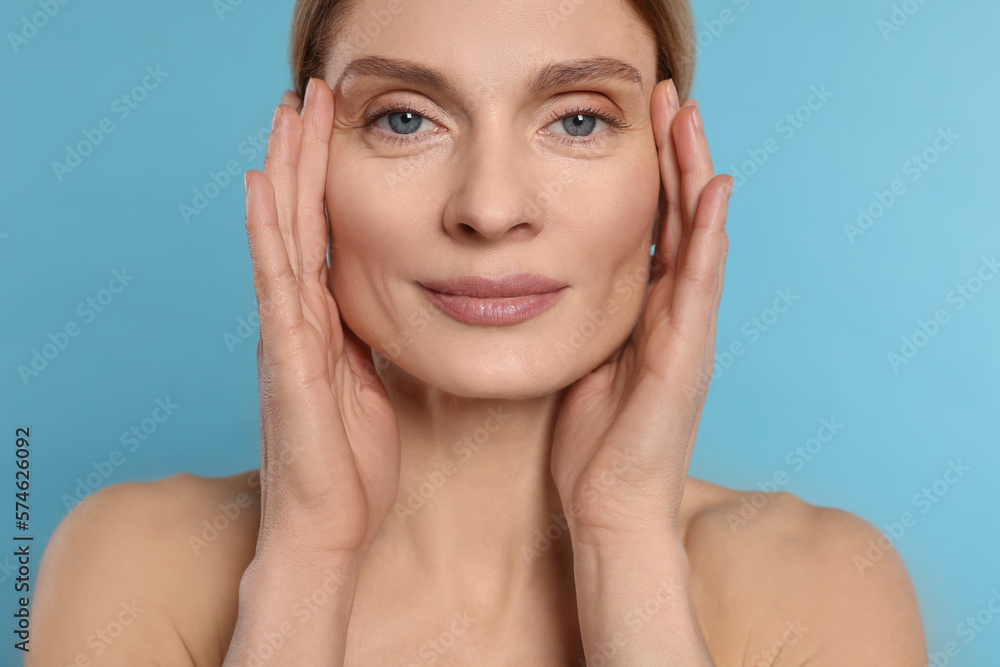 Woman massaging her face on turquoise background Woman massaging her face on turquoise background
