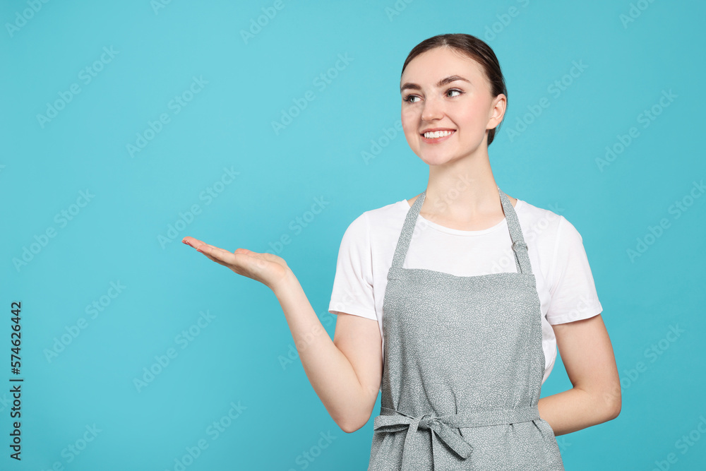 Beautiful young woman in clean apron with pattern on light blue background. Space for text Beautiful young woman in clean apron with pattern on light blue background. Space for text
