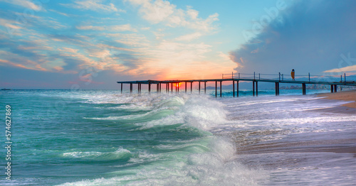 A woman standing on the pier watches the sunset - Long exposure photo of seascape with pier on a sunrise - Alanya  Turkey