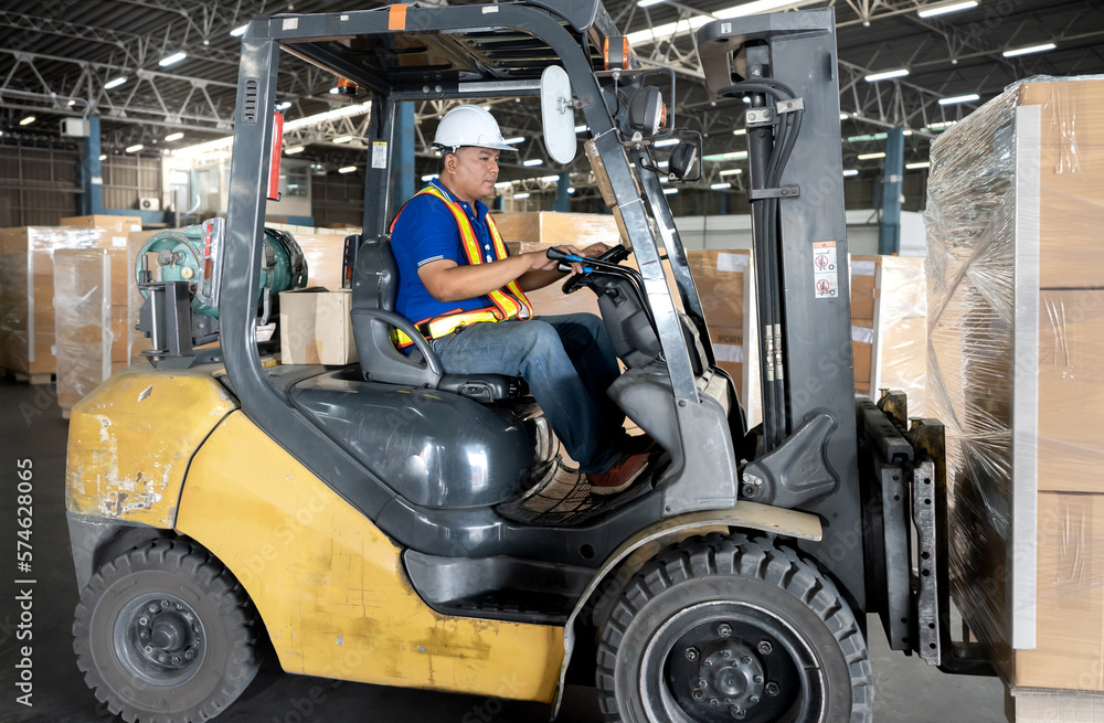 Male warehouse worker is driving a forklift in logistic distribution. Asian man driver wears hardhat is working in lifting cargo and shipment delivery at distribution warehouse—driver occupation.