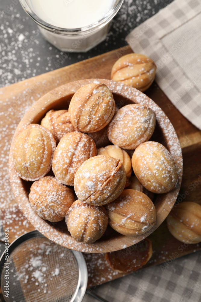 Delicious nut shaped cookies with powdered sugar and milk on black table, flat lay