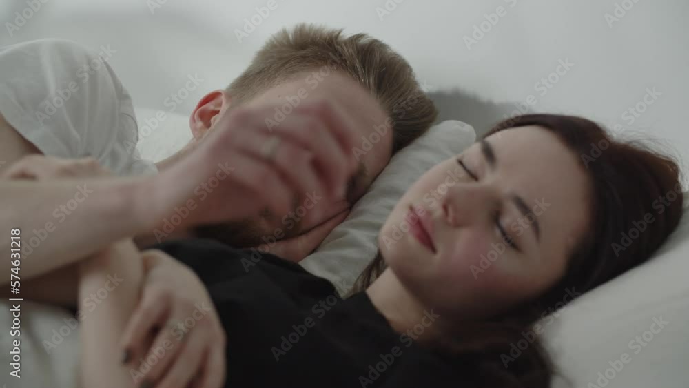 Man looking at his sleeping wife and touching her hair. Young couple cuddles in bed. Bearded guy lying next to his girlfriend Man looking at his sleeping wife and touching her hair. Young couple cuddles in bed. Bearded guy lying next to his girlfriend