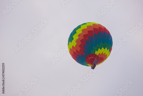 Colorful rainbow hot air balloon flying against grey sky at Winter aerostat festival, snow falling. Freedom, sport, aircraft concept