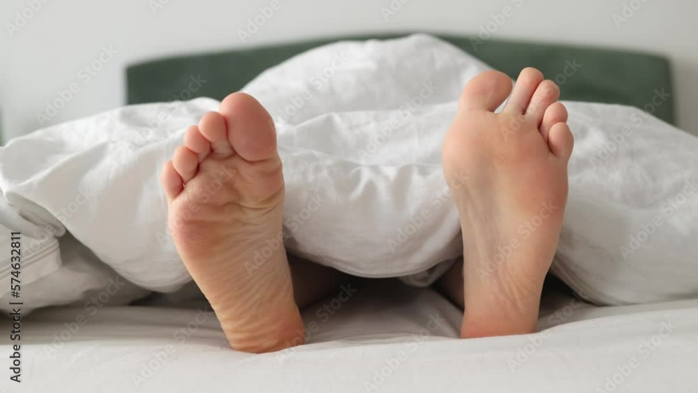 Woman's barefoot in close-up, funny shaking from side to side, lying on bed. Dry soles. Concept of vacation and rest. Woman's barefoot in close-up, funny shaking from side to side, lying on bed. Dry soles. Concept of vacation and rest.
