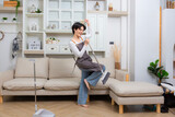 Full length shot of cheerful young woman, cleaning lady pretending to sing a song with holding broom while cleaning the floor.