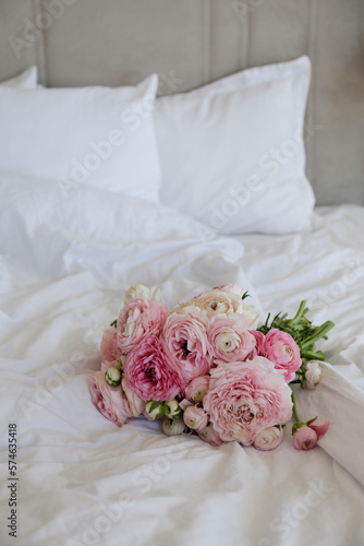 A beautiful bouquet of peonies and ranunculus flowers on the empty unmade bed with white sheets. A romantic surprize for st. Valentine's day. Close up, copy space, background, top view, natural light