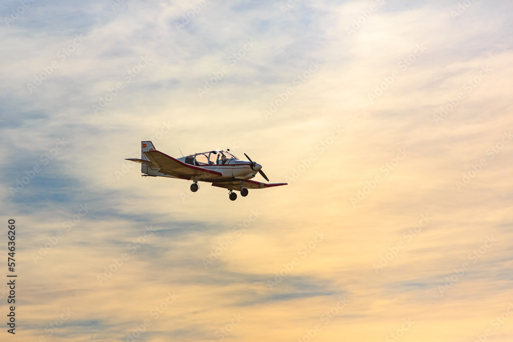 Single-engine airplane flies against the backdrop of sunset and the woman pilot waves her hand.