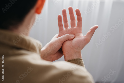 Close up back view of young man with shaking of Parkinson's disease, symptom of resting tremor, male holding hand to control hands tremor, neurological disorders, brain problems, health care concept