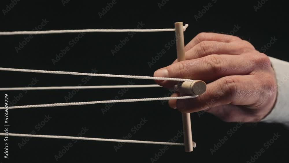 The puppeteer's hand controls the puppet with a wooden manipulator and strings. The marionettist controls and pulls the strings on a black isolated background. Vertical video. Close up. The puppeteer's hand controls the puppet with a wooden manipulator and strings. The marionettist controls and pulls the strings on a black isolated background. Vertical video. Close up.