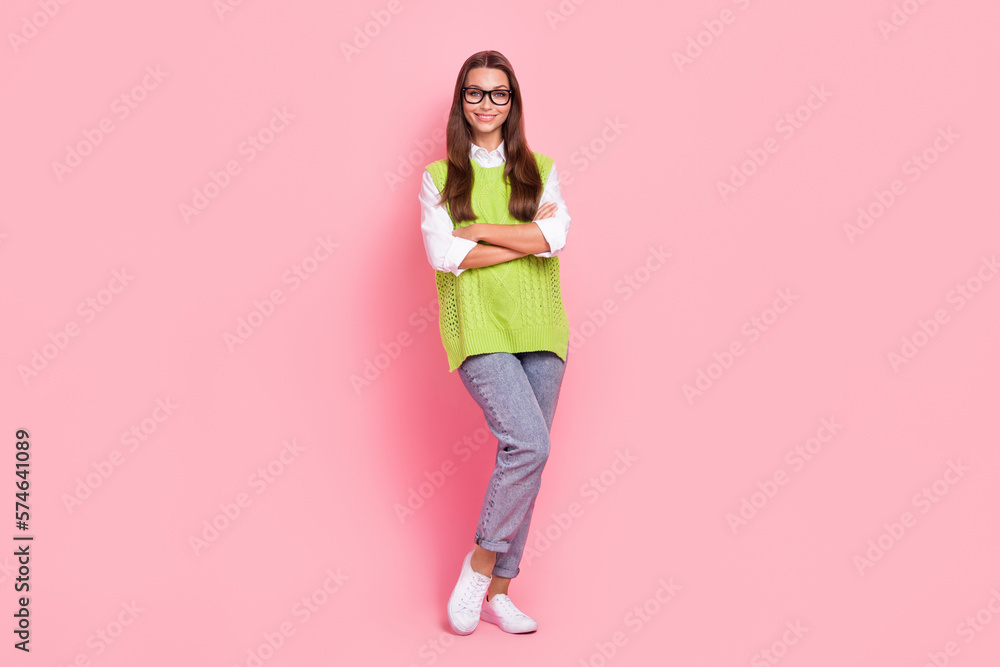 Full size photo of adorable pretty woman wear green waistcoat jeans sneakers holding arms crossed isolated on pink color background Full size photo of adorable pretty woman wear green waistcoat jeans sneakers holding arms crossed isolated on pink color background
