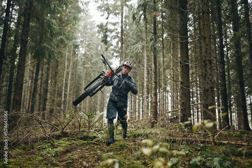 Lone rider carrying his mountain bike through the woods photo