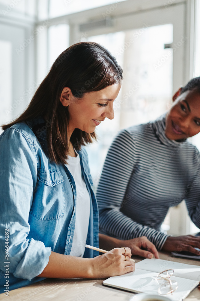 Smiling female entrepreneurs discussing notes together Smiling female entrepreneurs discussing notes together