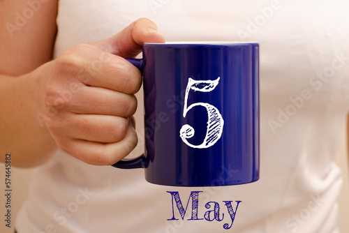 The inscription on the blue cup 5 may. Cup in female hand, business concept