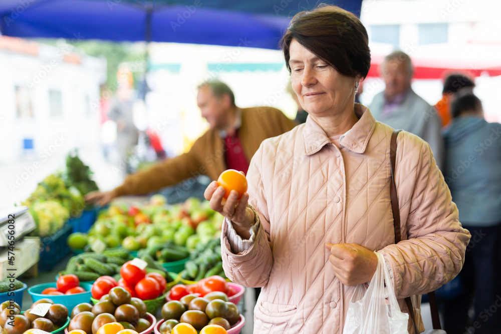 Fototapeta premium Aged woman customer buying vegetables in open-air market
