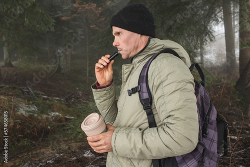 Man in the forest with a thermal mug and vape