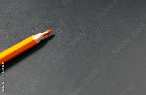 An orange pencil on a black piece of paper. Paper background, layout, template, place for text. Selective focus, copy space.