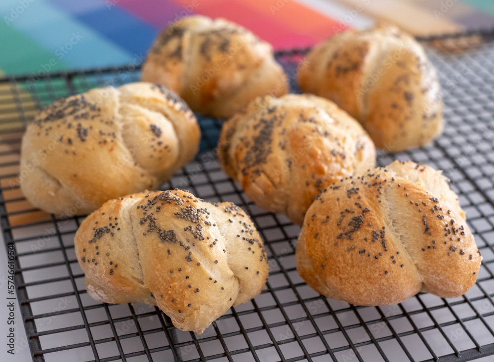 Traditional Jewish Challah knotted bread rolls for Shabbat, topped with poppy seeds, cooling on a wire tray.