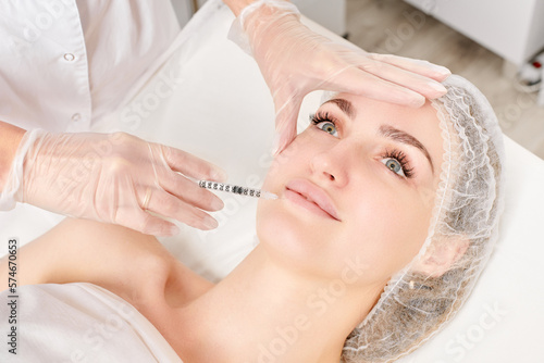Cosmetologist makes fillers injection for lips augmentation and volume, non surgical cosmetic procedure in beauty salon. Beautician specialist hands in gloves makes treatment injection with syringe photo