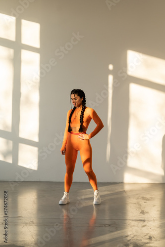 Beautiful young woman with natural make-up, dressed in a orange sports uniform, posing in the studio on a white wall.Advertising sportswear and yoga wear. Healthy lifestyle, sport