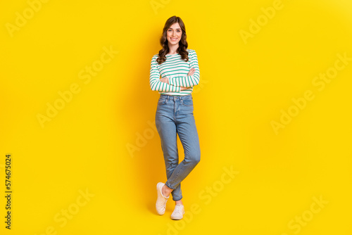 Full length photo of pleasant adorable girl wavy hairdo dressed striped shirt hold arms crossed isolated on yellow color background