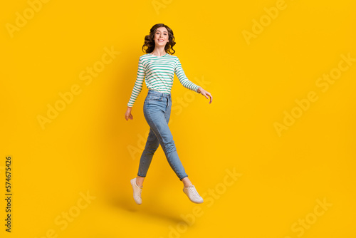 Full length photo of pleasant optimistic cute girl wear striped shirt denim pants flying dancing isolated on yellow color background