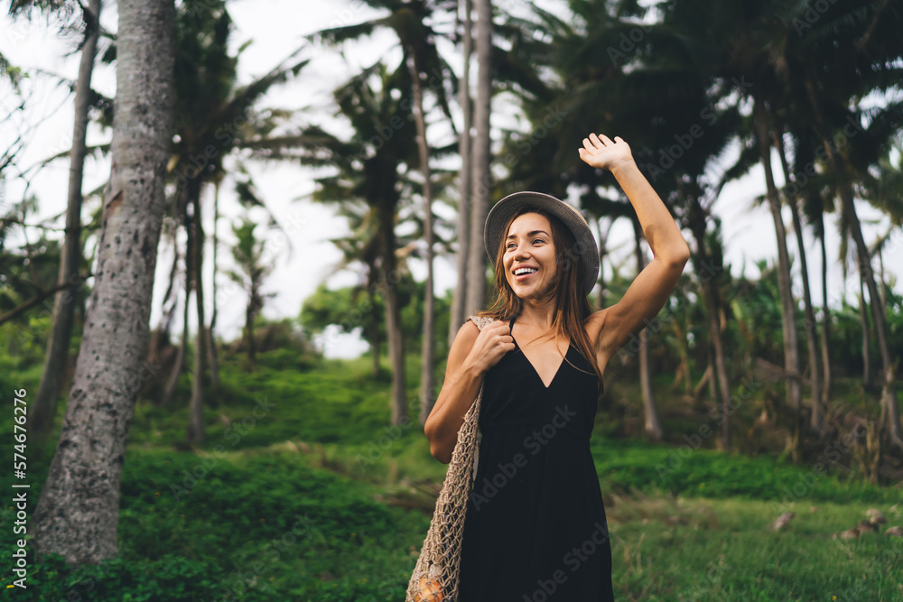 Happy woman standing and smiling with raised arm in park Happy woman standing and smiling with raised arm in park
