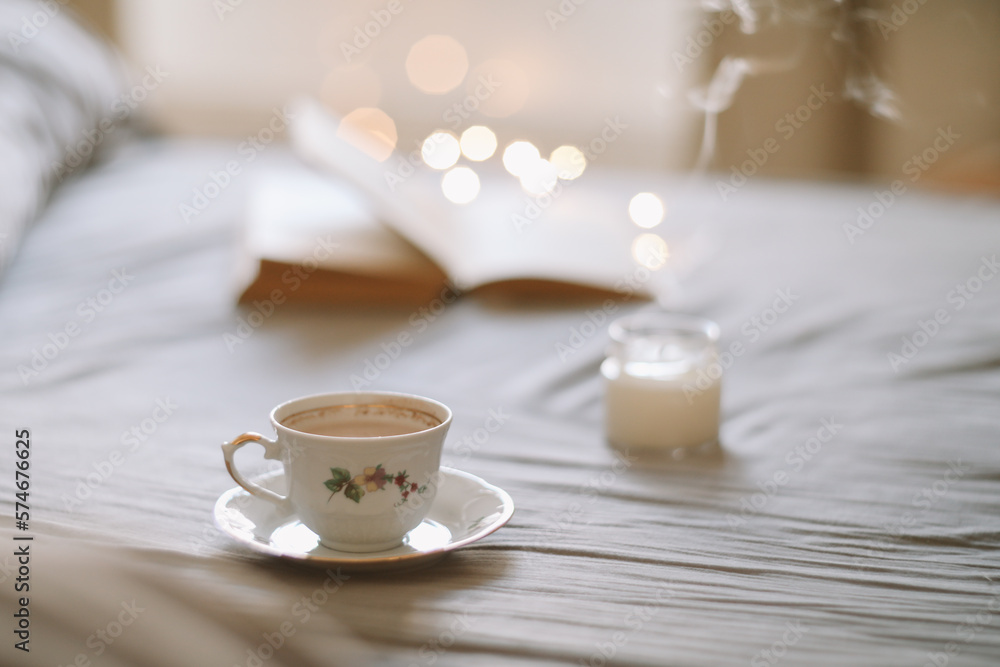 Light cozy bedroom, Coffee or tea cup and an open book on the bed. Spring still life. Breakfast in bed. Light cozy bedroom, Coffee or tea cup and an open book on the bed. Spring still life. Breakfast in bed.