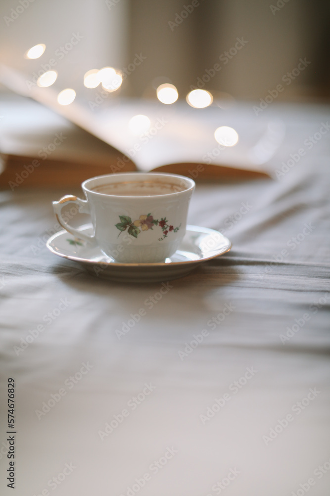 Light cozy bedroom, Coffee or tea cup and an open book on the bed. Spring still life. Breakfast in bed. Light cozy bedroom, Coffee or tea cup and an open book on the bed. Spring still life. Breakfast in bed.