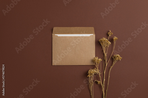 Mockup of a card made of eco-friendly kraft paper and decorated with a composition of dried meadow flowers arranged on a brown background