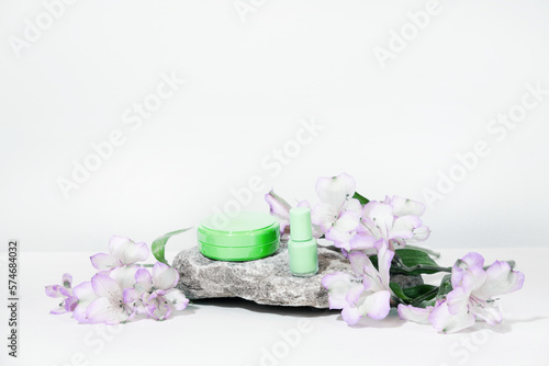 White cosmetics background. Cosmetic bottle containers with flowers plant . Blank label package for branding mock-up, with hard shadows. Natural organic beauty product concept.