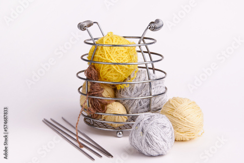This striking image captures a collection of small multicolored balls of knitting yarn inside a metal vase with iron spokes, set against a clean white backdrop.