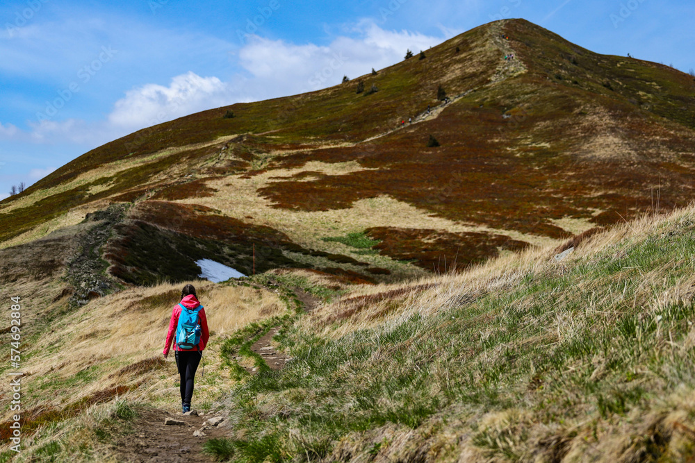 Fototapeta premium Beautiful fit happy girl in pink jacket enjoys hike in stunning colorful mountain scenery. Spring in the Bieszczady Mountains, Poland, Europe
