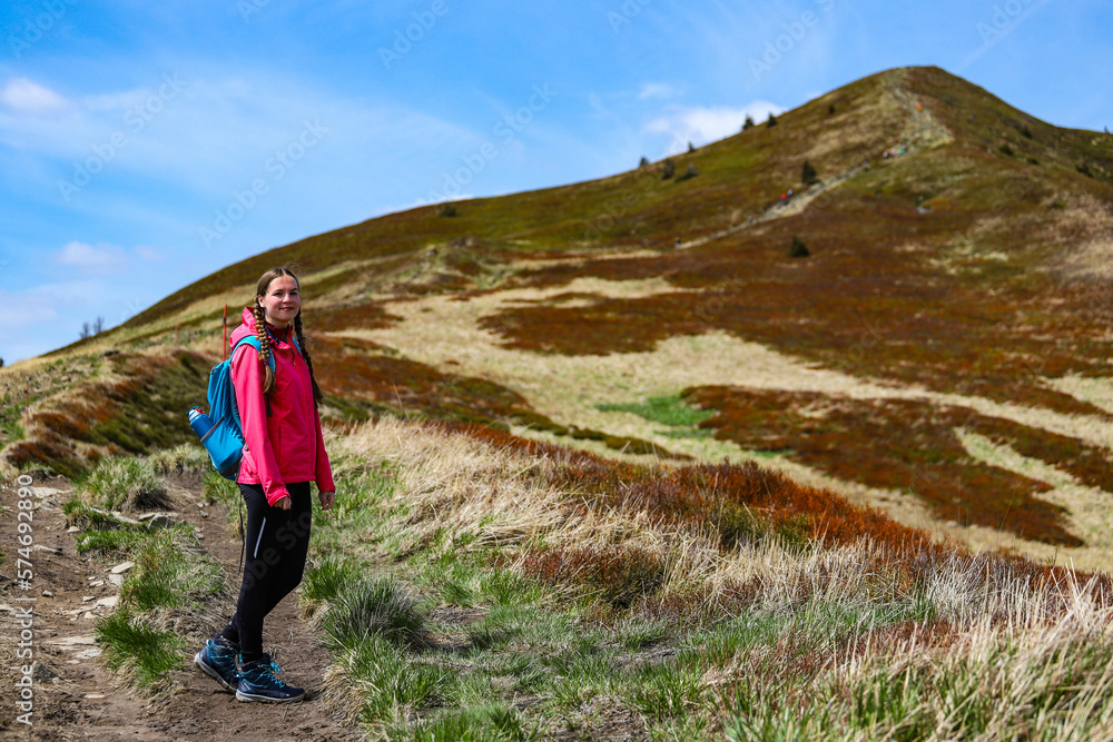 Beautiful fit happy girl in pink jacket enjoys hike in stunning colorful mountain scenery. Spring in the Bieszczady Mountains, Poland, Europe