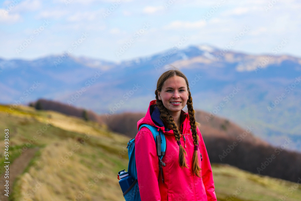 portrait of a beautiful, cute girl with braids standing at the top of the mountain during spring, hiking in the mountains with vegetation getting up to life, spring hiking