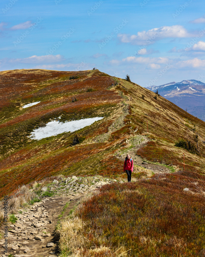 girl in pink jacket walks along a mountain ridge during spring; mountain walk with vegetation coming to life, colourful spring in the mountains