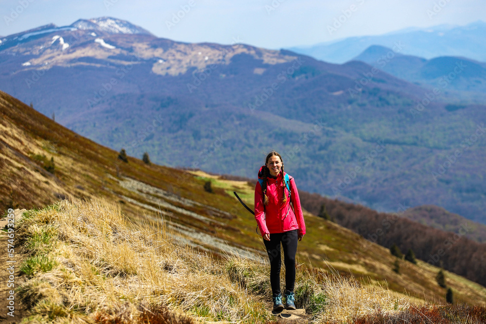 girl in pink jacket walks along a mountain ridge during spring; mountain walk with vegetation coming to life, colourful spring in the mountains