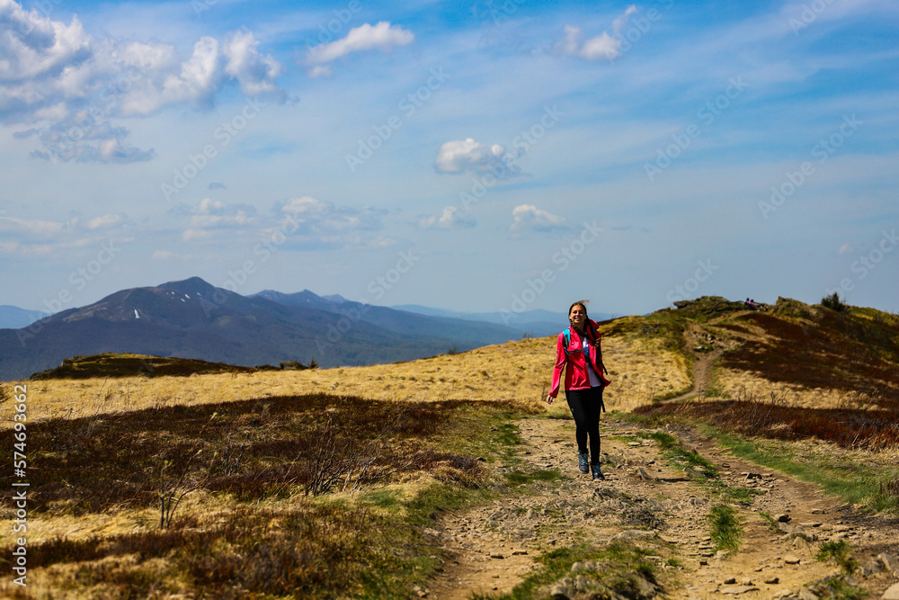 Fototapeta premium Beautiful fit happy girl in pink jacket enjoys hike in stunning colorful mountain scenery. Spring in the Bieszczady Mountains, Poland, Europe