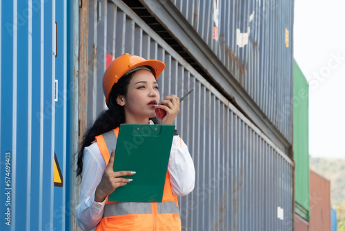 Smiling portrait of beautiful asian female industrial engineer wearing white helmet, vest holding walkie talkie. Safety Supervisor at Container Terminal