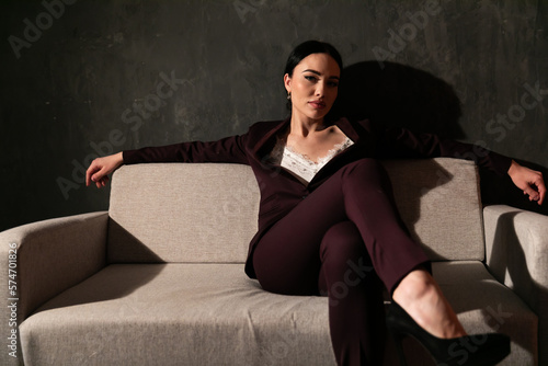 a woman in a business suit sits in a room on a sofa